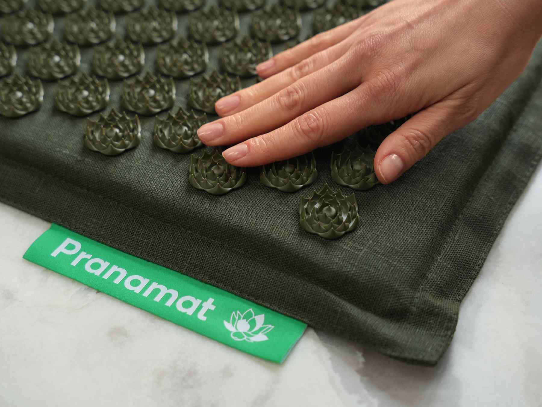 A hand pressing the lotus spikes of an olive Pranamat mat