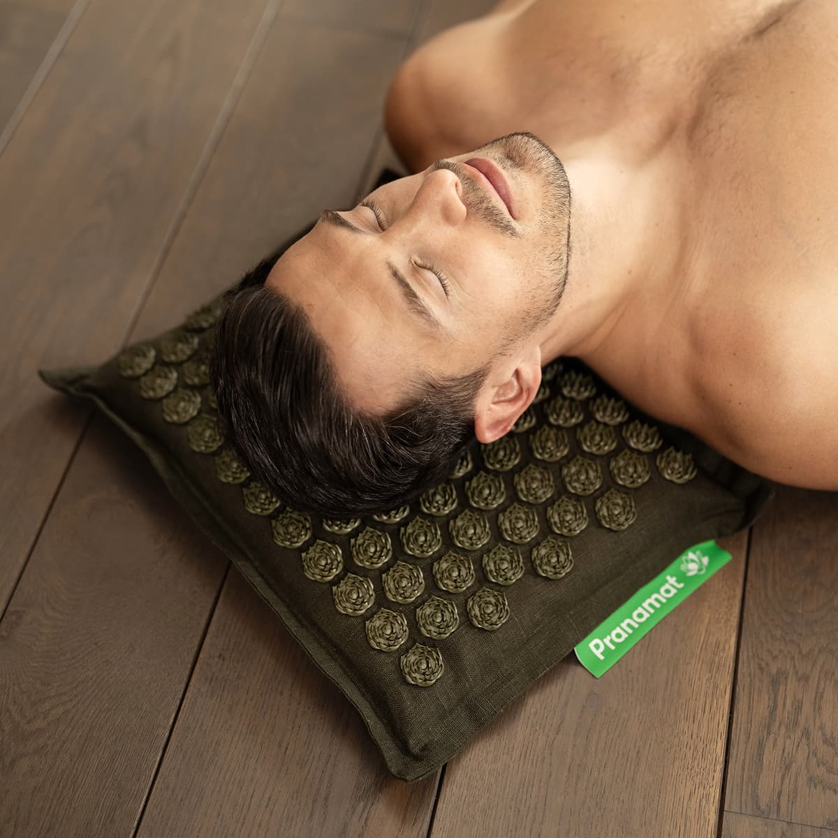 A man resting his head on the olive Pranamat pillow